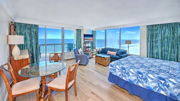 Habitación de hotel con balcón, una mesa de comedor, sofá, cama y televisión.