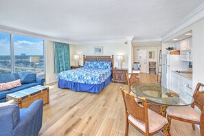 A hotel room with a bed, a sofa, a dining table with chairs, a kitchen area, and a large window. - Oceanfront King Studio w/Balcony| Newly Remodeled (Daytona Beach)