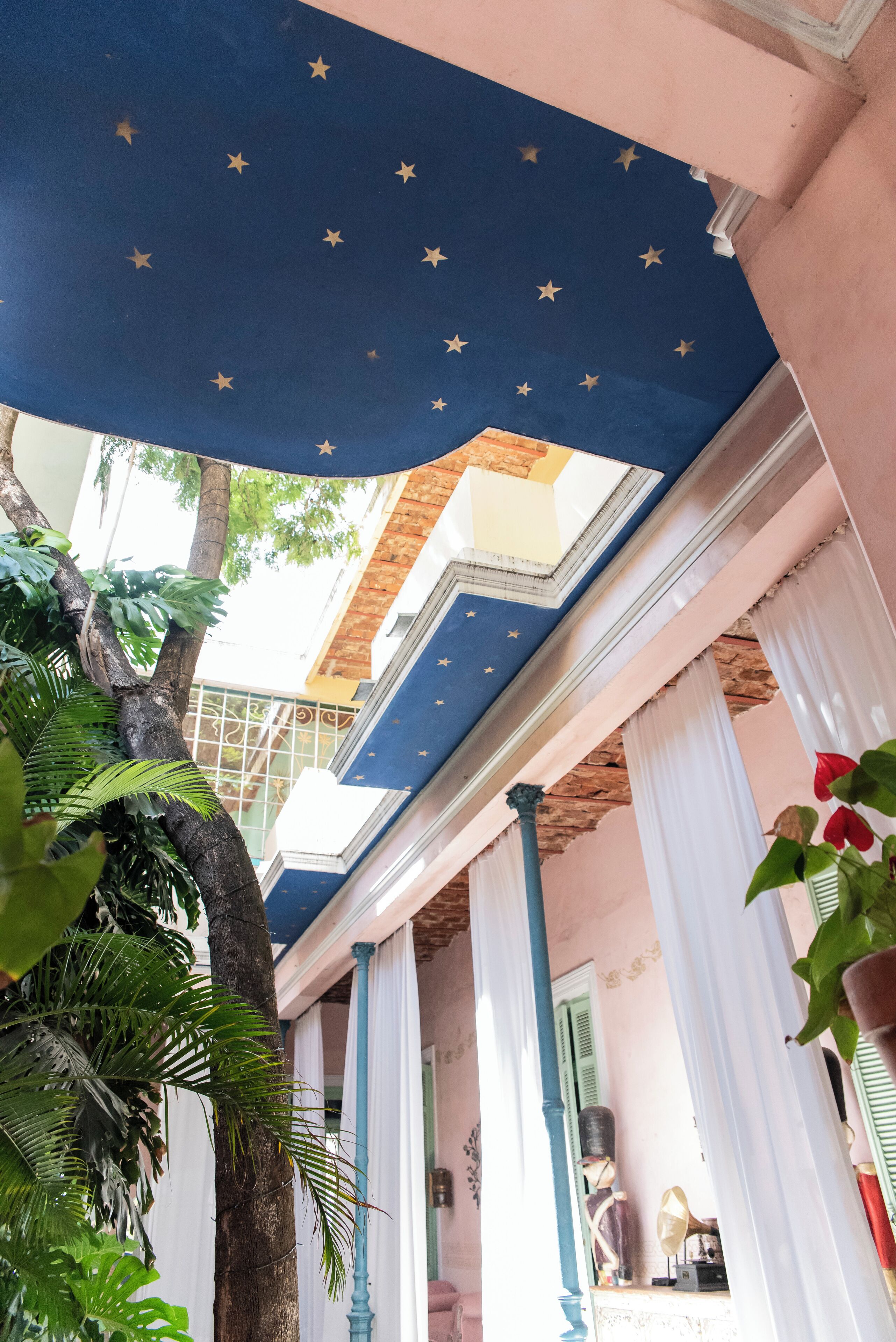 A room with a blue ceiling decorated with stars, white columns, and a view of the outside.