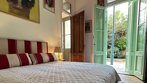 Et soveværelse med en stor seng, et natbord med lampe, en dør til en balkon og et maleri på væggen.