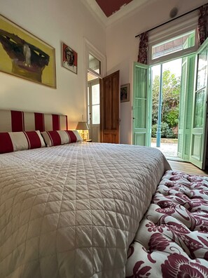 Un dormitorio con una cama grande, una mesita de noche con lámpara, una puerta que da a un balcón y un cuadro en la pared.