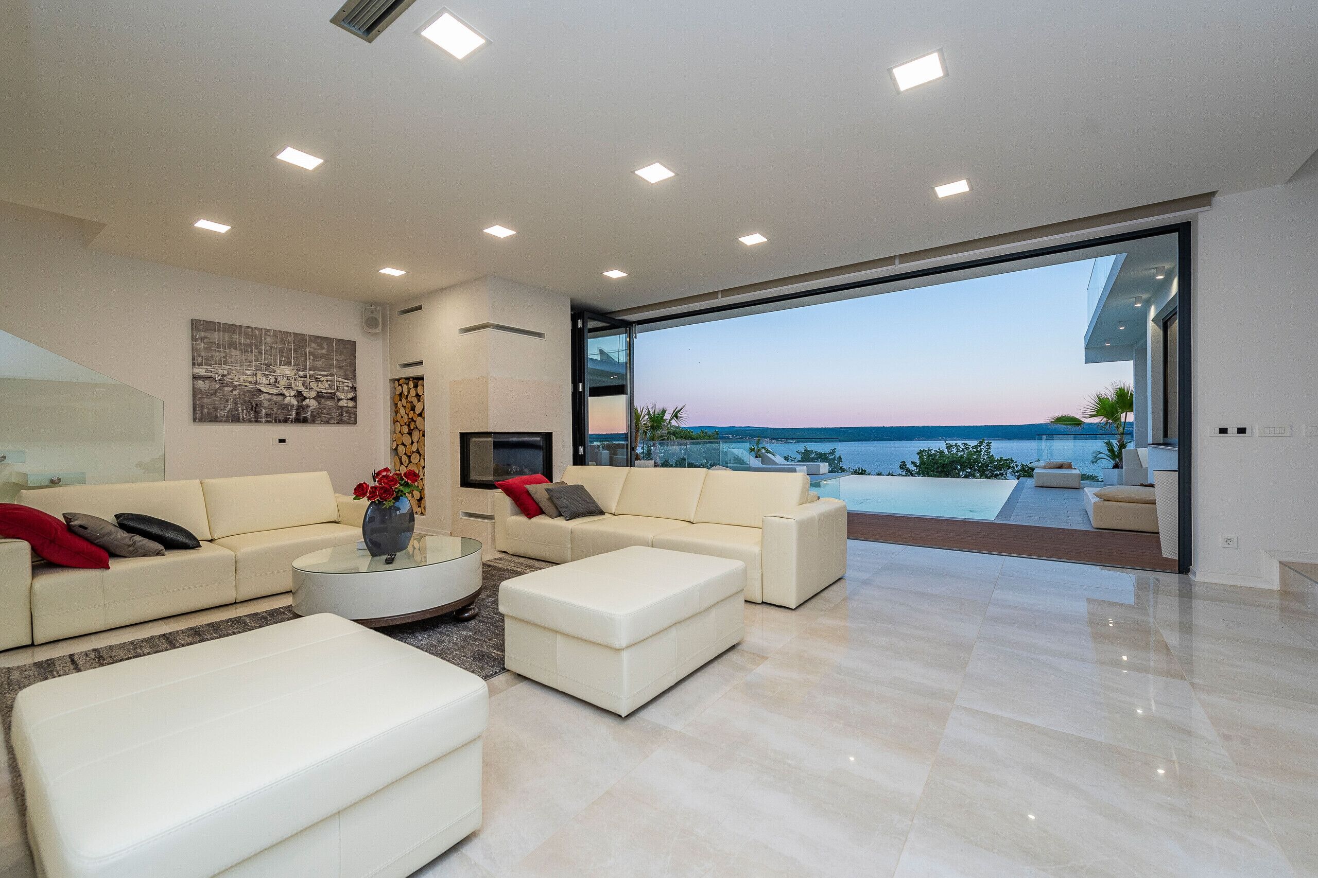 A modern living room with a large glass door leading to a balcony with a view of the sea.