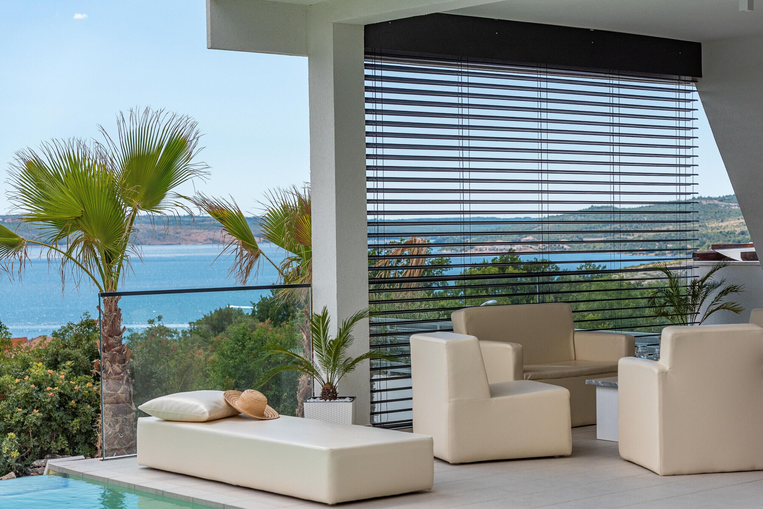A modern outdoor lounge with a pool, white furniture, and a view of the sea.