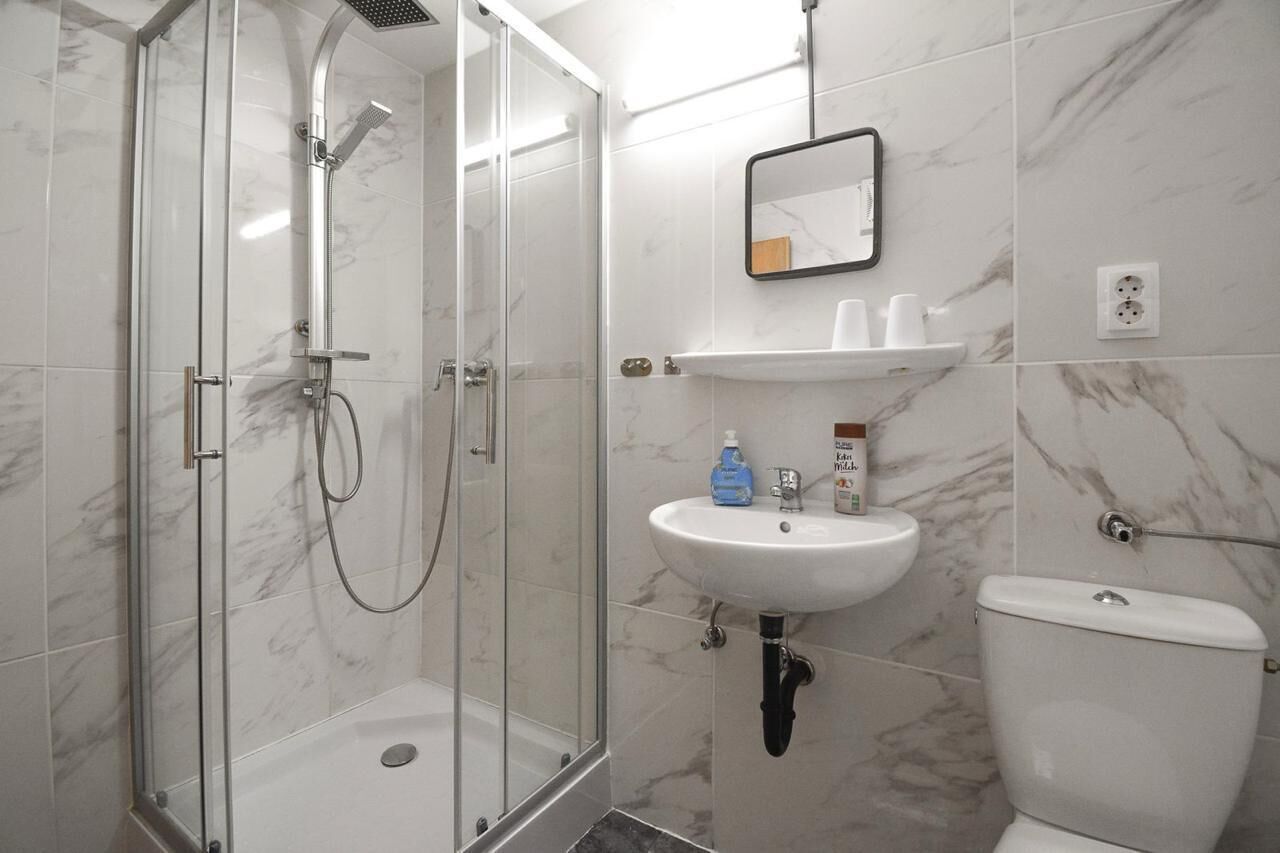 A bathroom with a glass-enclosed shower, a white sink, and a toilet.