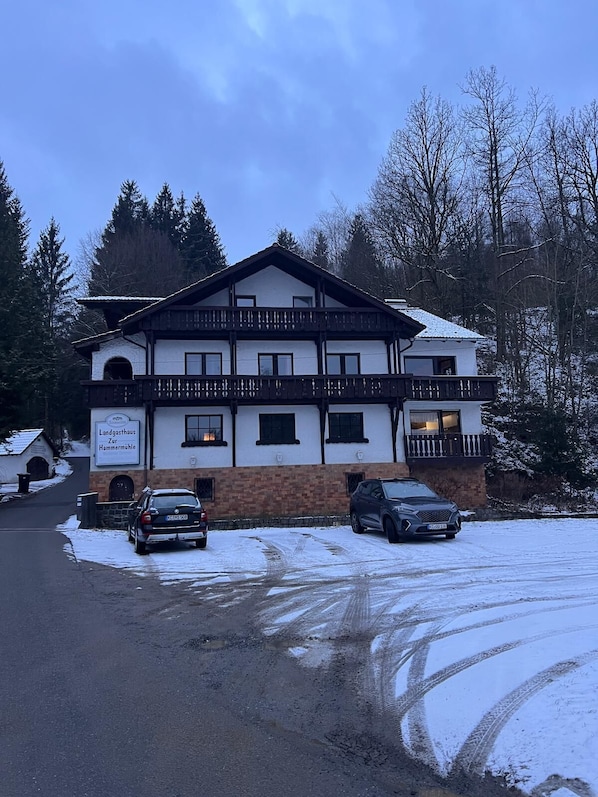 A two-story building with a sign reading "Landgasthaus Zur Hammermühle." There are two cars parked in front, and the ground is partially covered with snow. - Landgasthaus zur Hammermühle (Wallenfels)