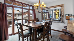 A dining area with a large wooden table, multiple chairs, and a chandelier. - Spacious, Multi-Floor 4bedroom Townhome Walking Distance to Village, Along Orient Chairlift! (Sun Peaks)