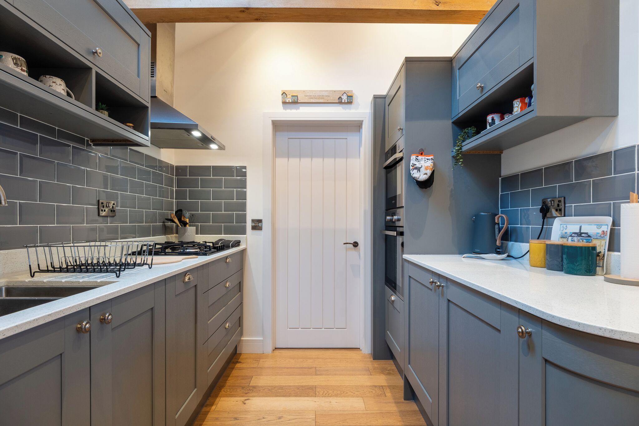 A modern kitchen with grey cabinets, a white door, and a tiled backsplash.