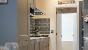 A modern kitchen with grey cabinets, a tiled backsplash, and a wooden ceiling beam. - Beautiful 2 Bedroom Barn in Cerney Wick (Cirencester)