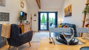 A modern living room with a dining area, wooden beams, a TV, and a view of the outdoors. - Beautiful 2 Bedroom Barn in Cerney Wick (Cirencester)