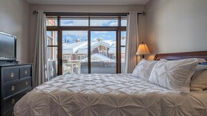 Una camera d'albergo con un letto grande, una cassettiera, una televisione e una finestra che si affaccia su edifici e un paesaggio innevato.