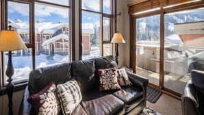 Un accogliente soggiorno con divano in pelle, cuscini decorati e ampie finestre che offrono vista su un paesaggio innevato e palazzi.