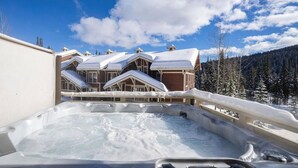 Una vasca idromassaggio con vista su un edificio in stile chalet e alberi innevati sullo sfondo.