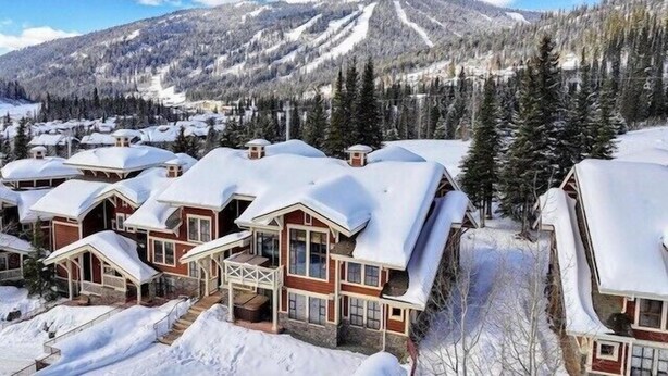 Un gruppo di edifici in stile chalet con tetti innevati, sullo sfondo di una montagna innevata e di una fitta foresta.