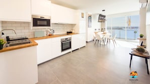 A modern kitchen with white cabinetry, a wooden countertop, and a dining area with a round table and chairs.