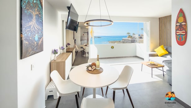 A modern dining area with a view of the sea, a large abstract painting, and a surfboard decoration.