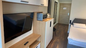 A compact room with a large flat-screen TV, a microwave, a small refrigerator, a bed, and a wooden cabinet. - Lovely 1-bedroom apartment in Bakuriani perfect for a cozy getaway (Bakuriani)