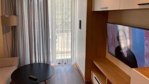 A modern living room with a flat-screen TV, a sofa, a coffee table, and a sliding glass door with curtains. - Lovely 1-bedroom apartment in Bakuriani perfect for a cozy getaway (Bakuriani)