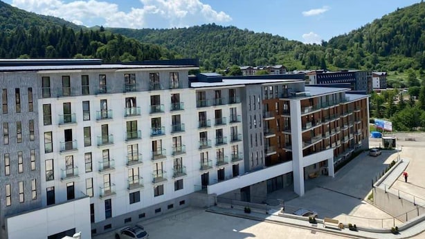 A multi-story hotel with a modern architectural design, featuring balconies and a parking area in front. - Lovely 1-bedroom apartment in Bakuriani perfect for a cozy getaway (Bakuriani)