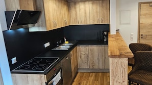 Een kleine keuken met houten kastjes, een zwart aanrecht, een ingebouwde kookplaat en een enkele stoel.