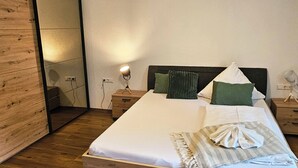 Een net opgemaakt bed met witte lakens, een houten hoofdbord en een nachtkastje met een lamp.