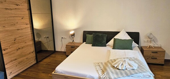 A neatly made bed with white linens, a wooden headboard, and a bedside table with a lamp.