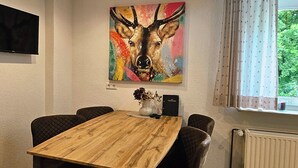 Een eetgedeelte met een houten tafel, vier stoelen, een schilderij van een hert, een flatscreen televisie en een raam met gordijnen.