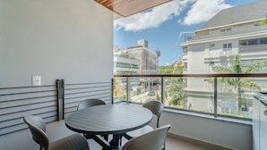A balcony with a round table and chairs, a power outlet, and a view of surrounding buildings. -  Apt w/ Barbecue Grill 50 m from the Beach DOI0203 (Florianópolis)