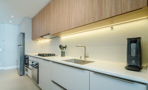 A modern kitchen with white cabinetry, stainless steel appliances, and a built-in coffee machine. -  Apt w/ Barbecue Grill 50 m from the Beach DOI0203 (Florianópolis)