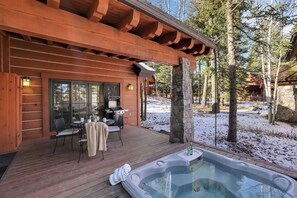 A wooden cabin with a hot tub, outdoor seating, and a stone fireplace.
