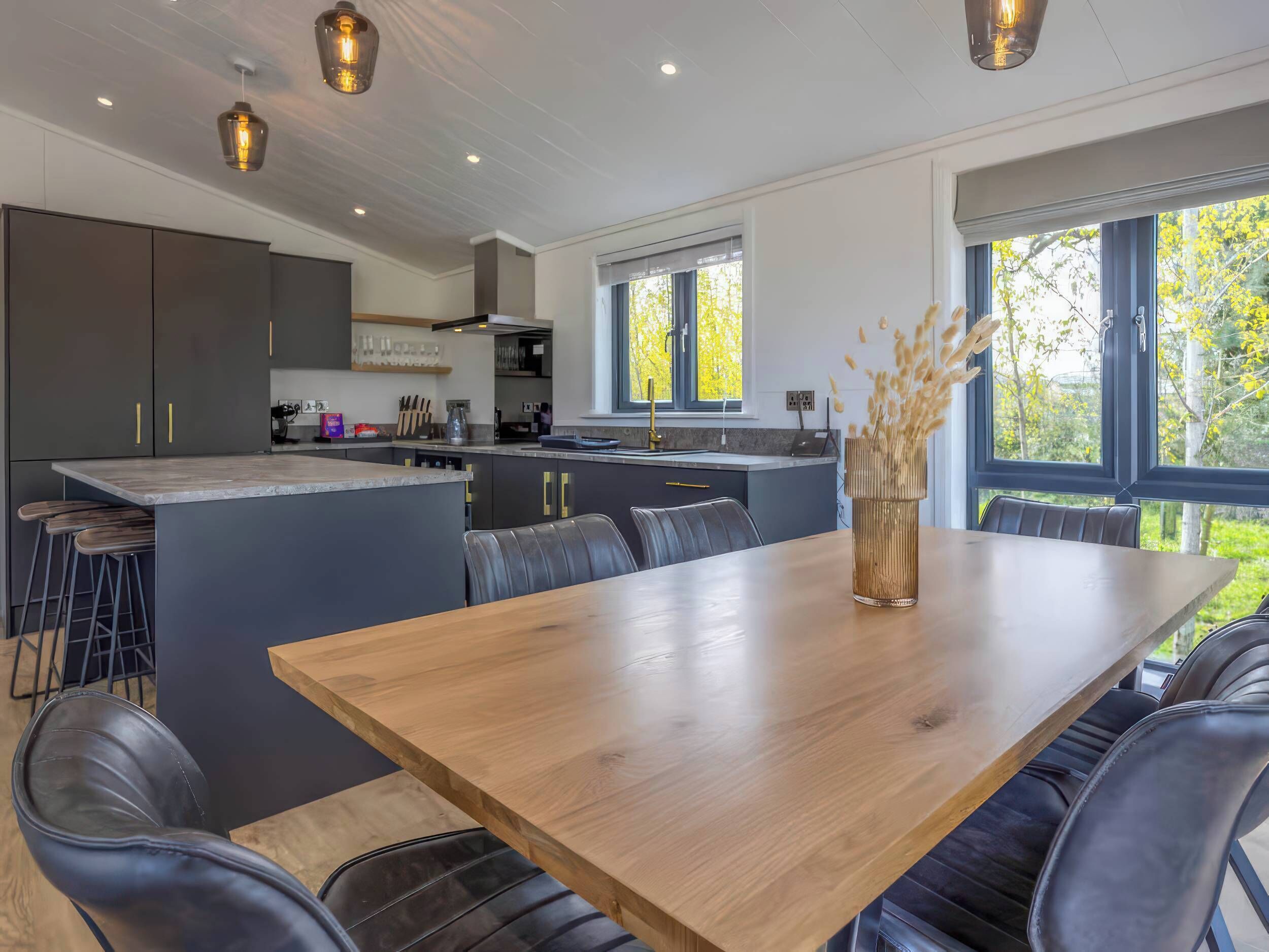 A modern kitchen with dark cabinets, a central island, and a dining area with a wooden table and leather chairs.