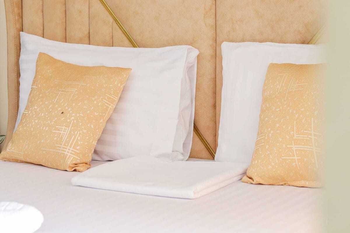 A bed with white bedding and two pillows, one with a textured pattern.