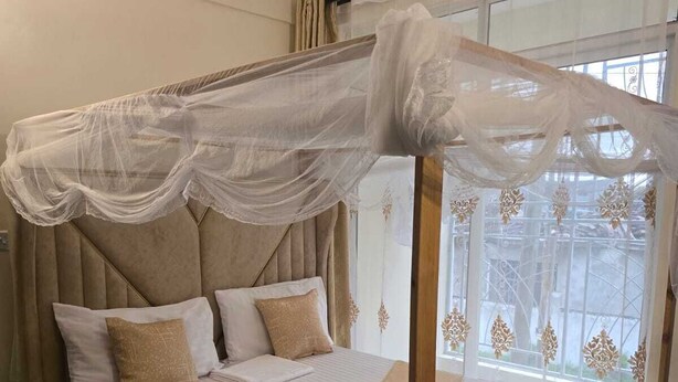 Una cama con dosel, un cabecero de madera y vistas al exterior a través de una ventana con cortinas decorativas.