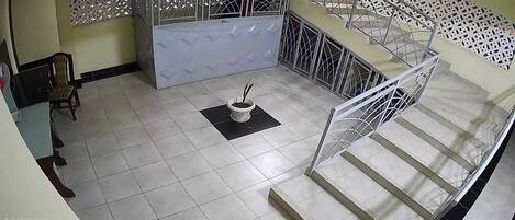 Una escalera con barandillas metálicas, una planta en maceta sobre un felpudo negro, y una silla en primer plano.