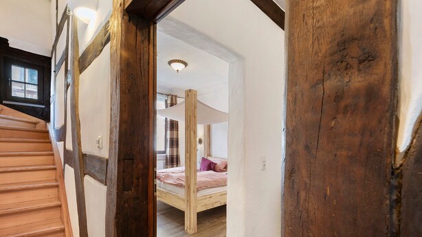 A wooden staircase leading to a room with a bunk bed, a window, and a ceiling light.