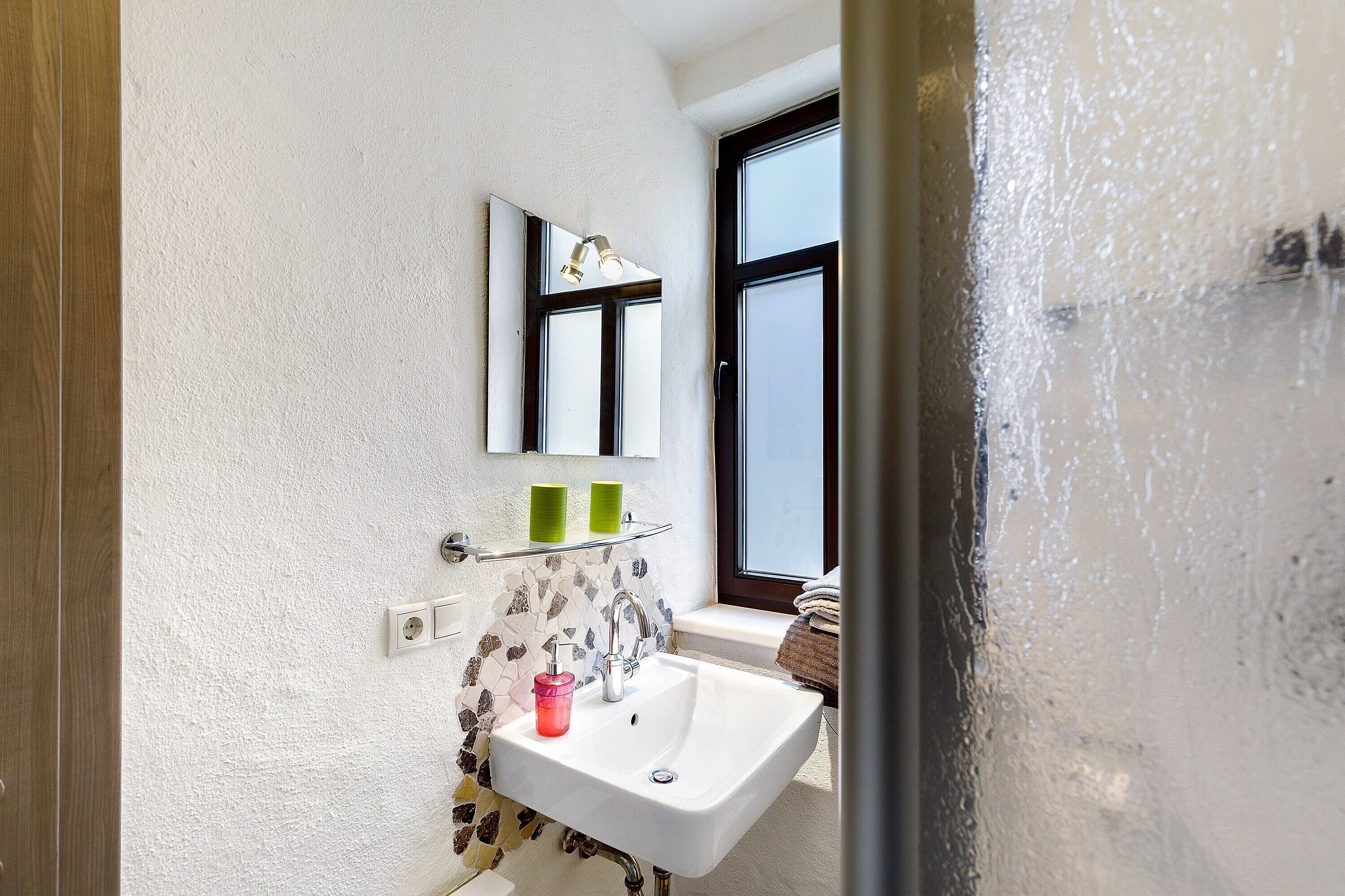 A bathroom with a white sink, a mirror, and a window.