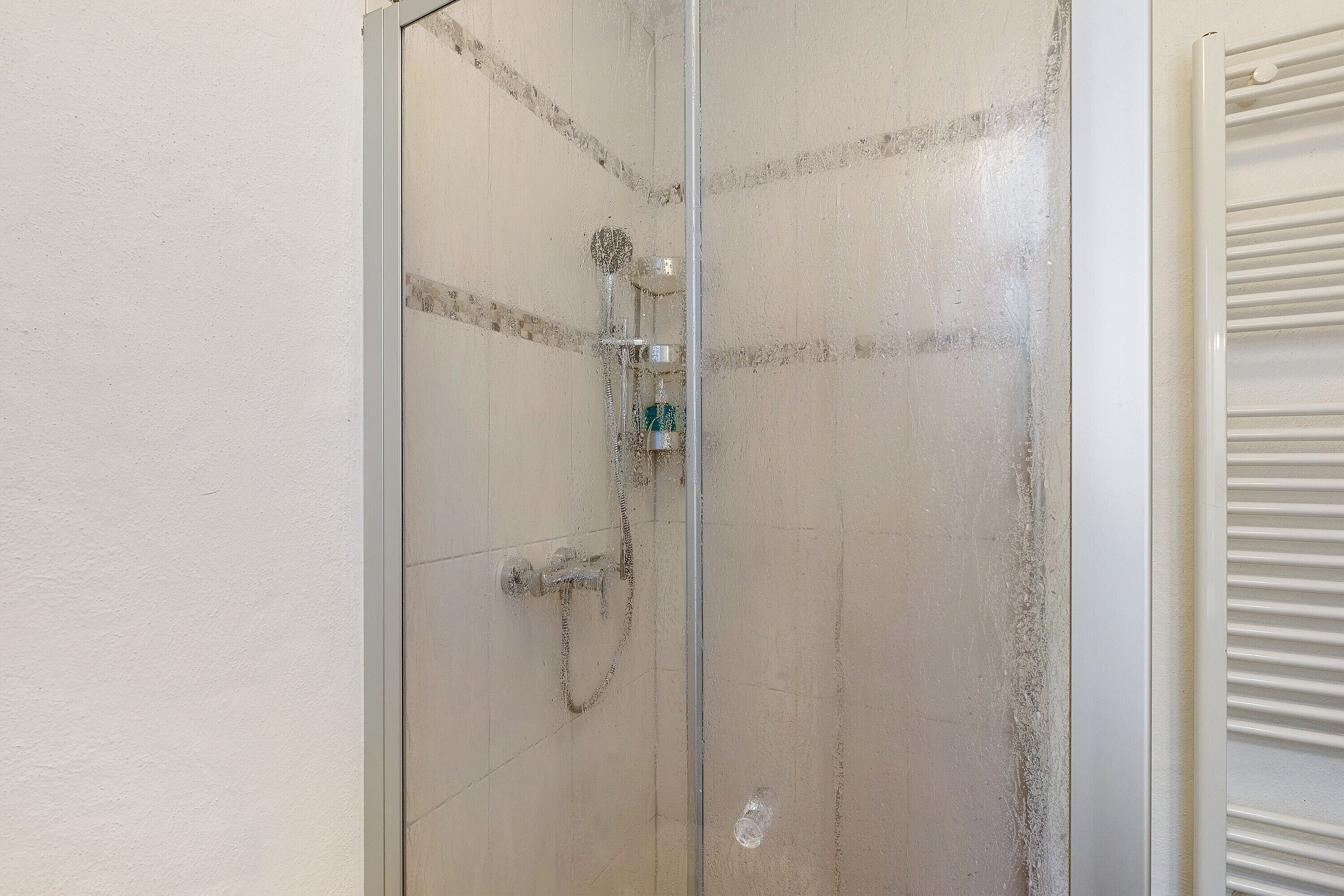 A glass-enclosed shower with a handheld showerhead and a wall-mounted faucet.
