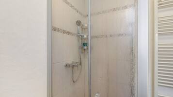 A glass-enclosed shower with a handheld showerhead and a wall-mounted faucet.