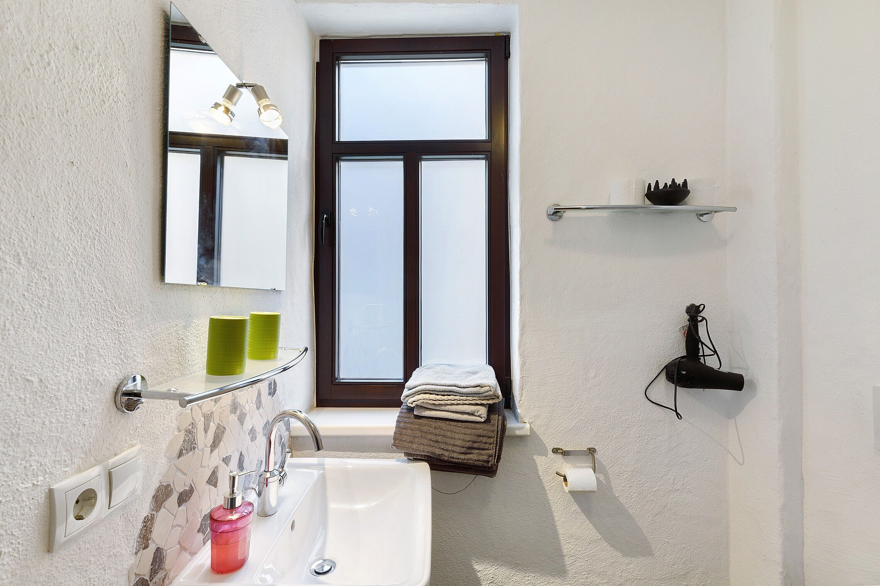 A bathroom with a white sink, a mirror, a towel rack, and a window.