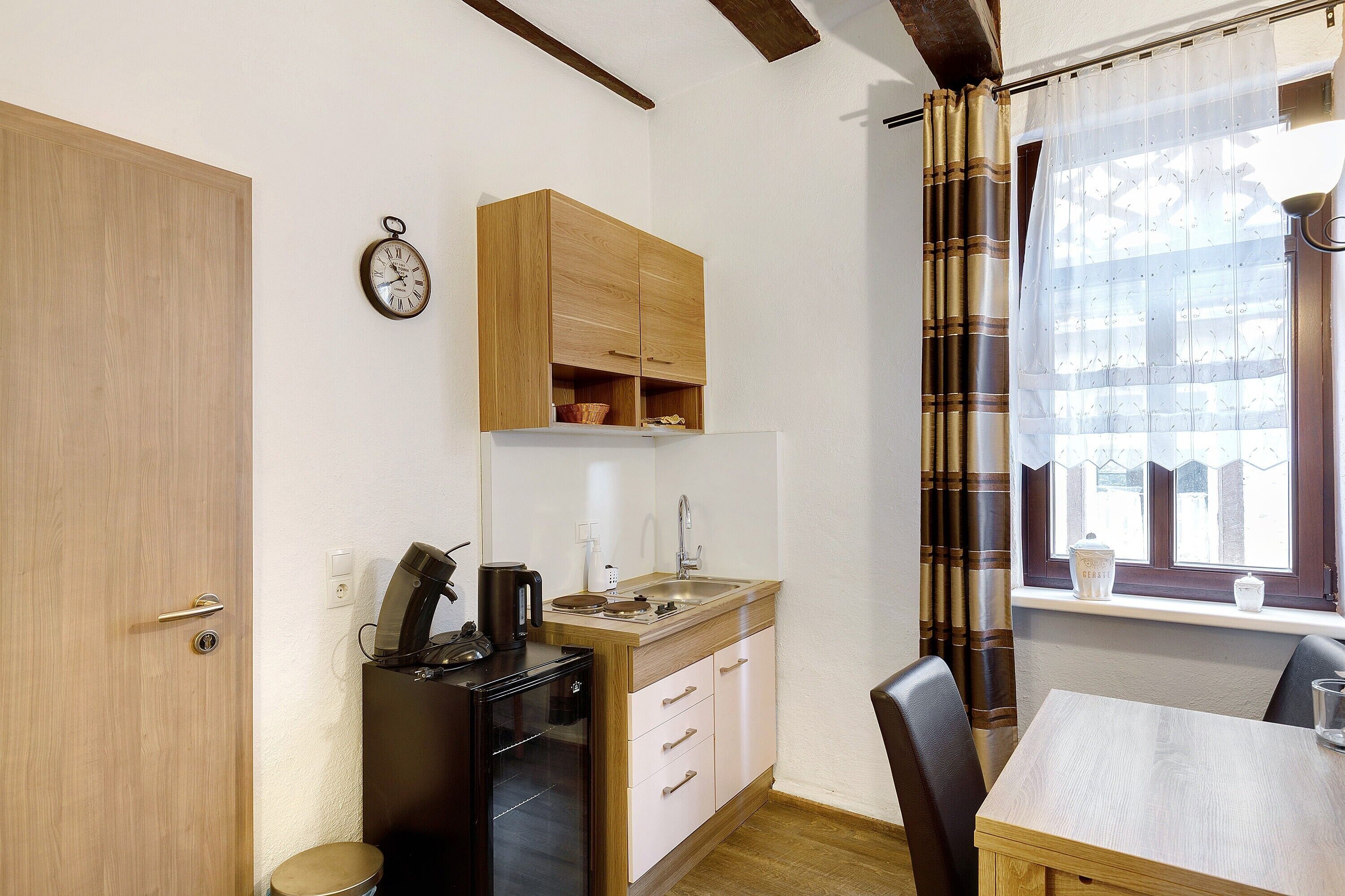 A compact kitchen with a sink, stove, and cabinets, a dining table with chairs, and a window with curtains.