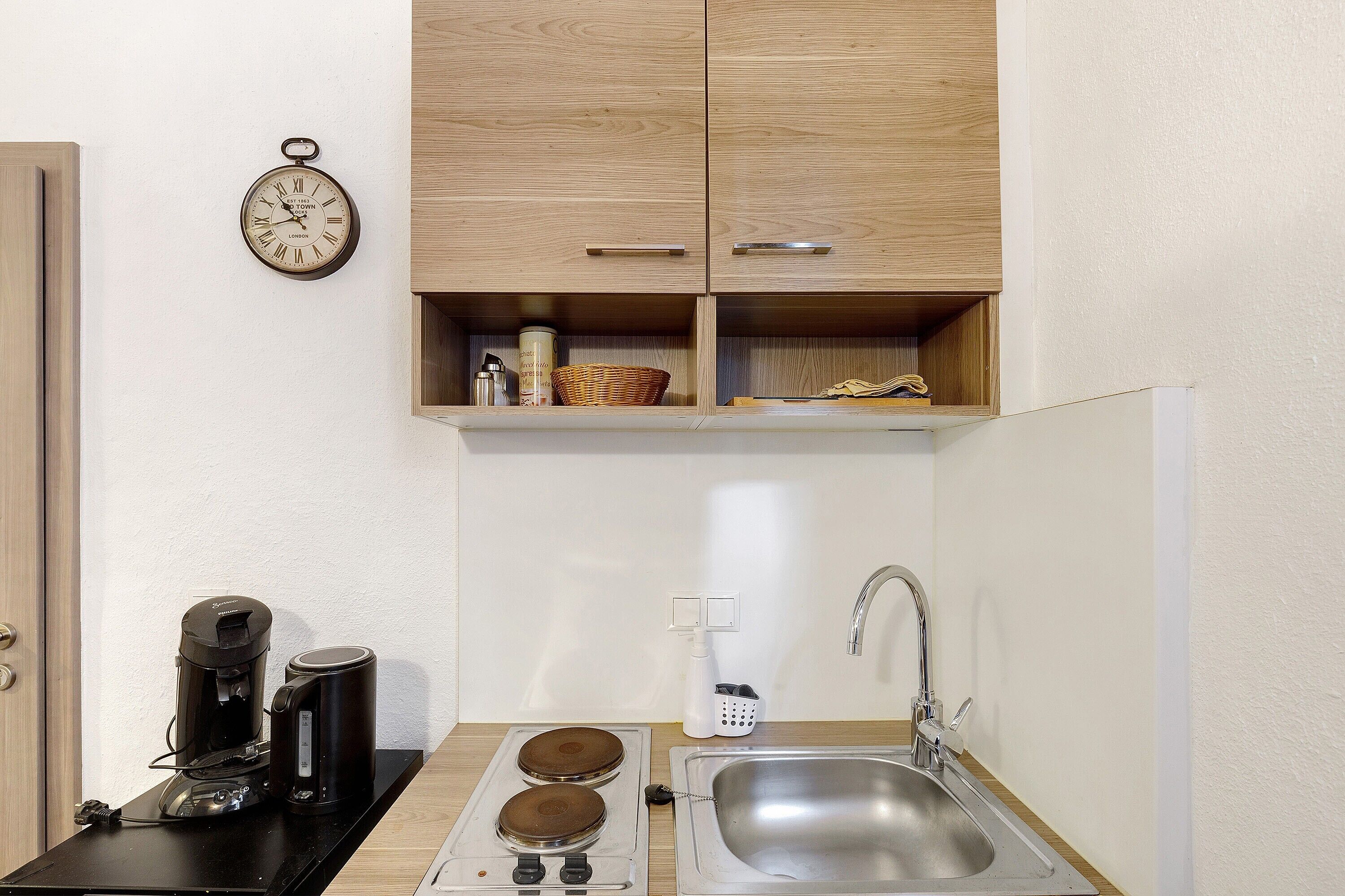 A compact kitchen with a coffee maker, kettle, and sink.