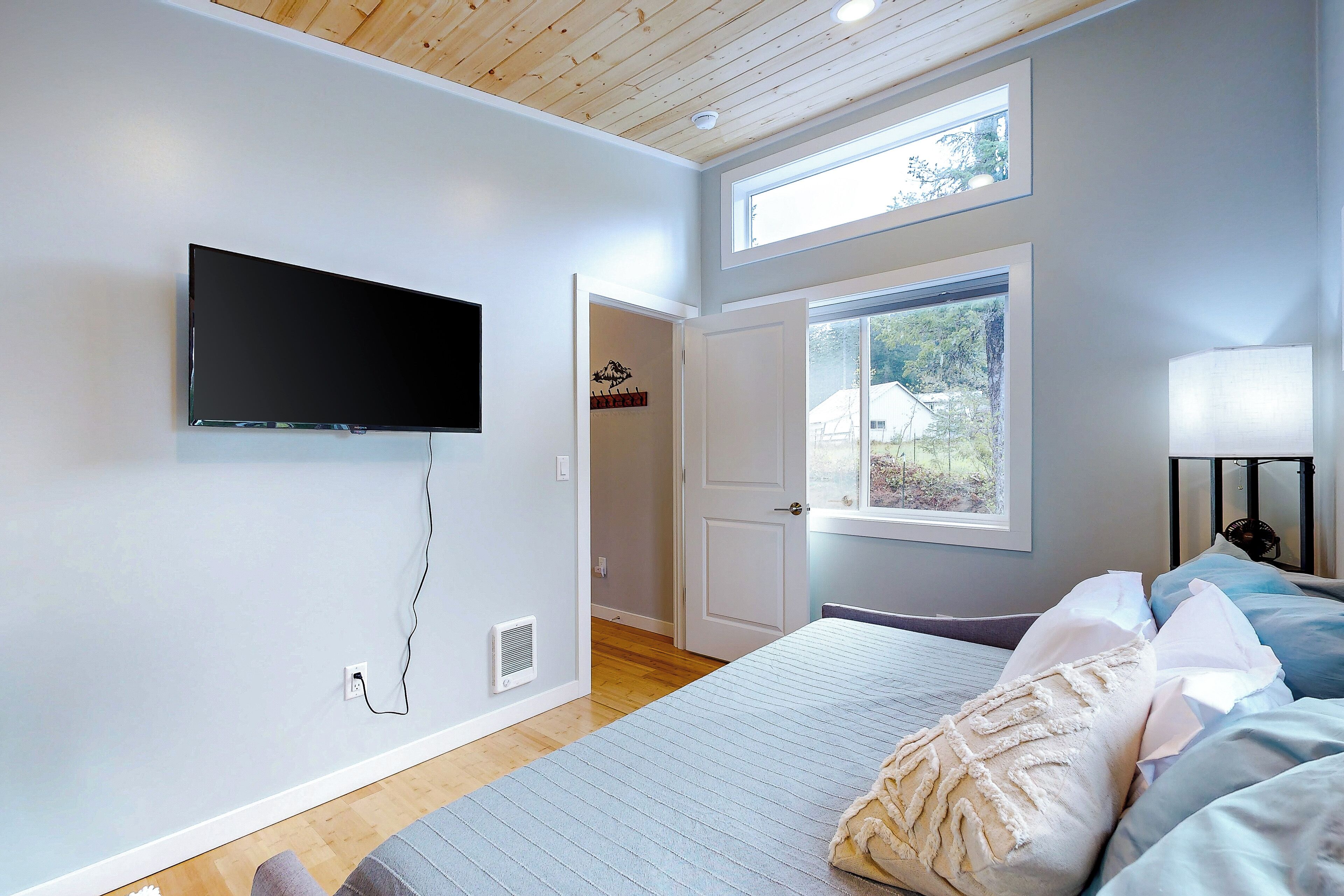 A bedroom with a bed, a TV mounted on the wall, a window, and a door leading to another room.