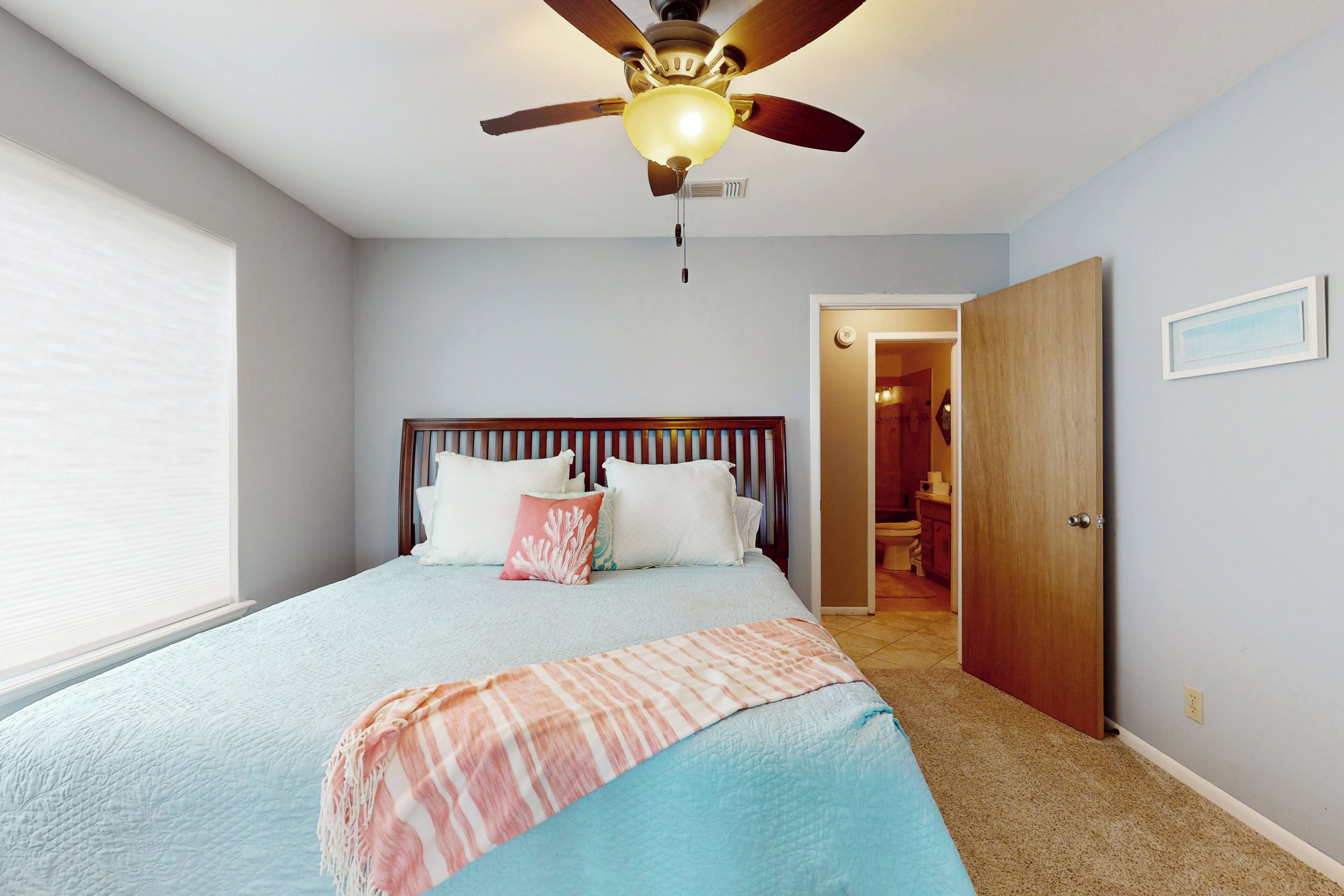 A bedroom with a bed, a ceiling fan, a door, and a window.