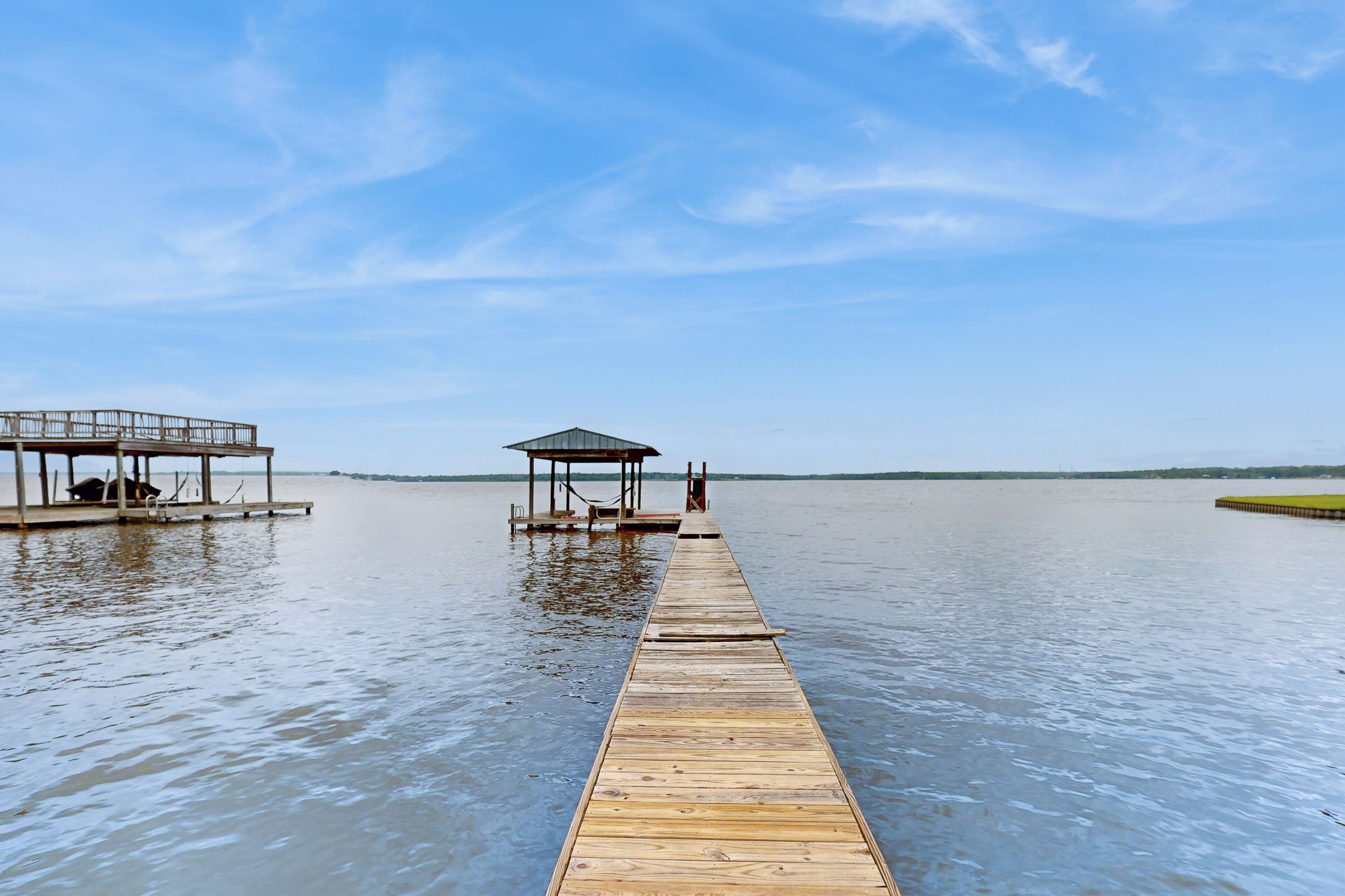 A wooden pier extending into calm water, with a covered seating area and a gazebo on the left.
