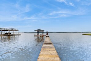 A wooden pier extending into calm water, with a covered seating area and a gazebo on the left.