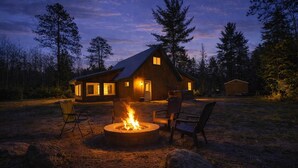 A rustic cabin with a fire pit, outdoor seating, and a view of the surrounding forest at dusk. - Hot Tub, Firepit, AC, Near Trails & Lakes (Phelps)