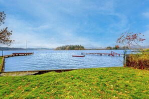 A lakeside view with a grassy foreground, a wooden dock, and a small boat on the water. - 2 BR Lakeside Home w/ Wood-burning Fireplace (Silver Lake)