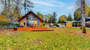 Une cabane en bois à deux étages, dotée d’une terrasse, entourée d’arbres et bordée d’une pelouse.
