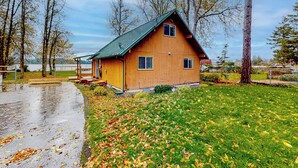 Une cabane en bois avec un toit vert, entourée d’une zone herbeuse et d’arbres.