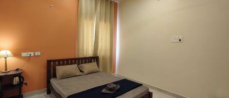 A bedroom with a bed, a nightstand, a lamp, a ceiling fan, and a window with curtains.