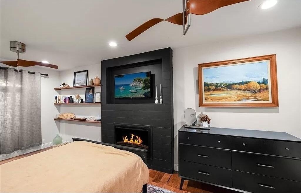 Een slaapkamer met een bed, een open haard, een plafondventilator, een televisie en kunst aan de muren.